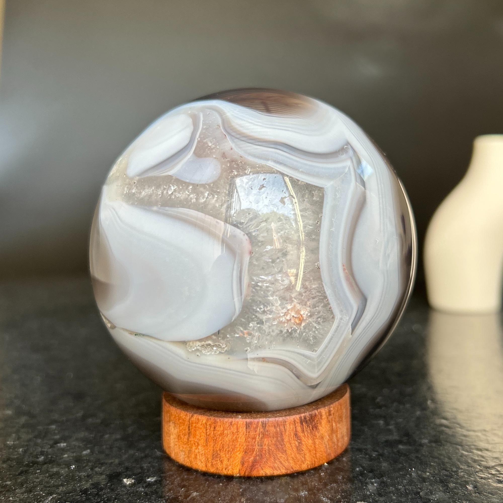 Polished agate sphere with clear, gray, and brown jasper and quartz formations on a carob wood base.