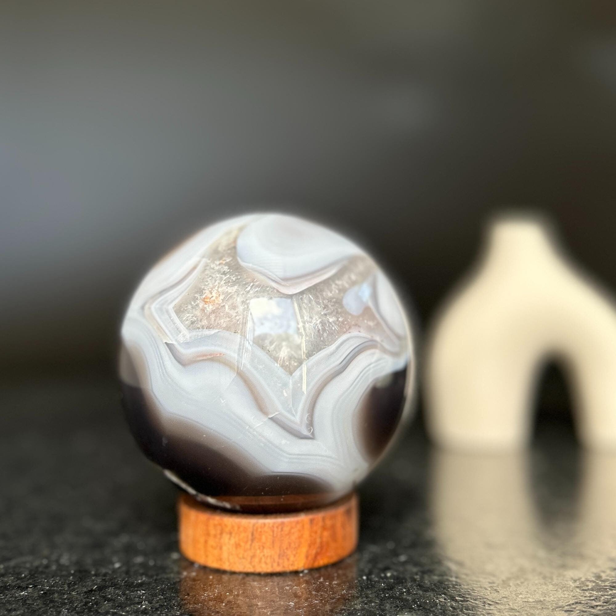 Polished agate sphere with clear, gray, brown jasper and quartz formations on a carob wood base.