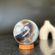 Agate sphere with clear, gray, and brown quartz formations on a carob wood base.