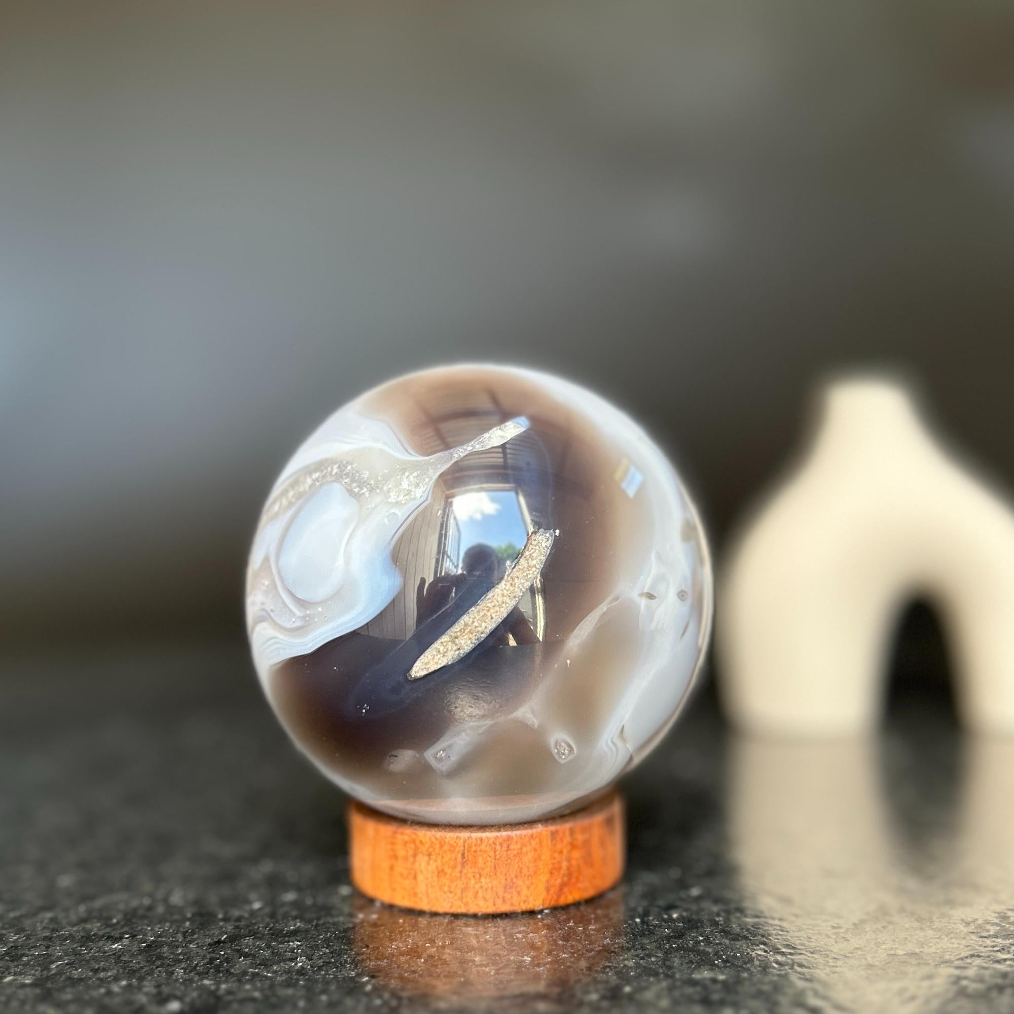 Agate sphere with clear, gray, and brown quartz formations on a carob wood base.