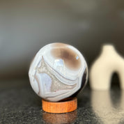 Polished agate sphere with clear, gray, and brown quartz formations on a carob wood base.