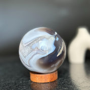 Polished agate sphere with clear, gray, and brown quartz formations on a carob wood base.