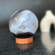 Polished agate sphere with clear, gray, and brown quartz formations on a carob wood base.