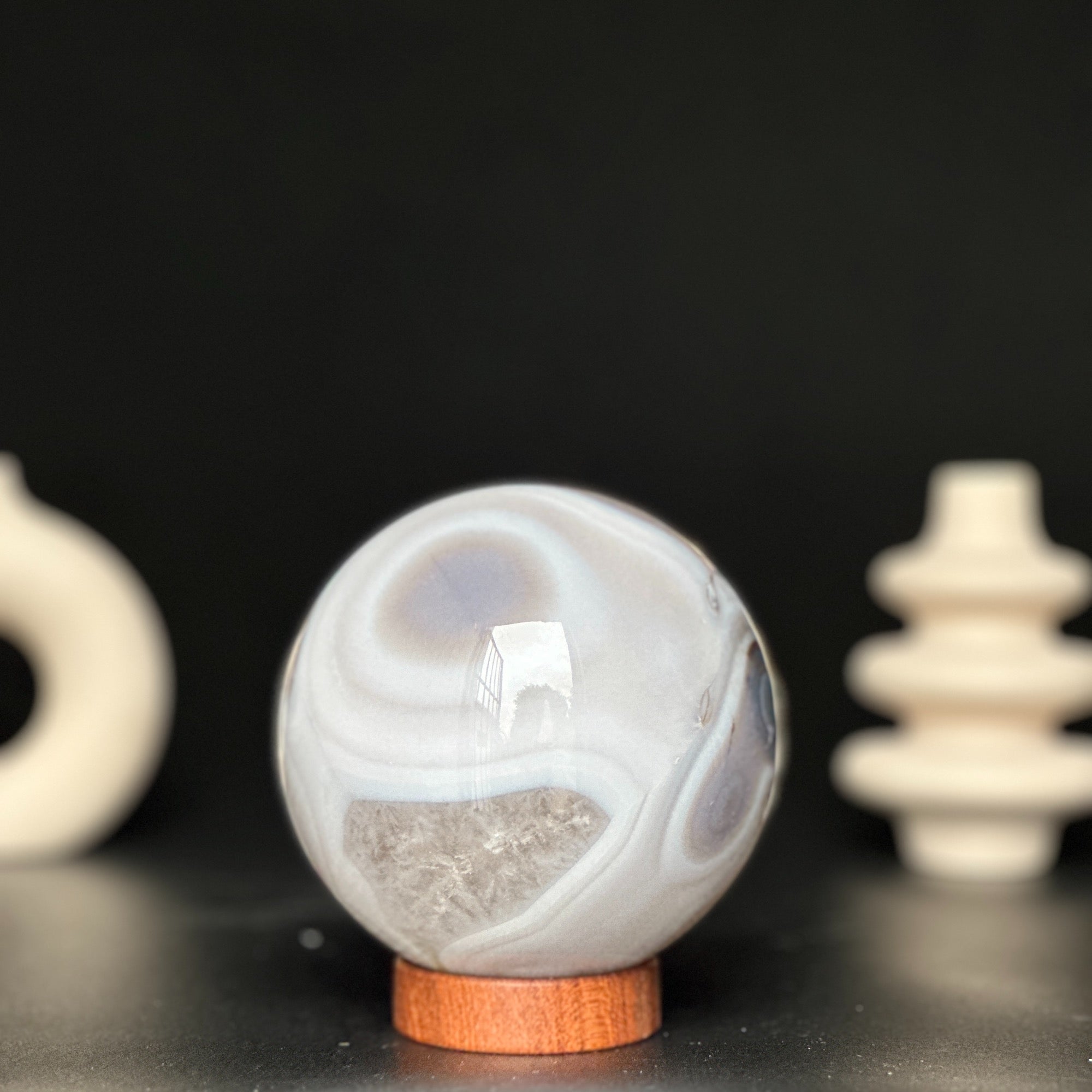 Polished white and beige agate sphere on a round carob wood base, with a black background.