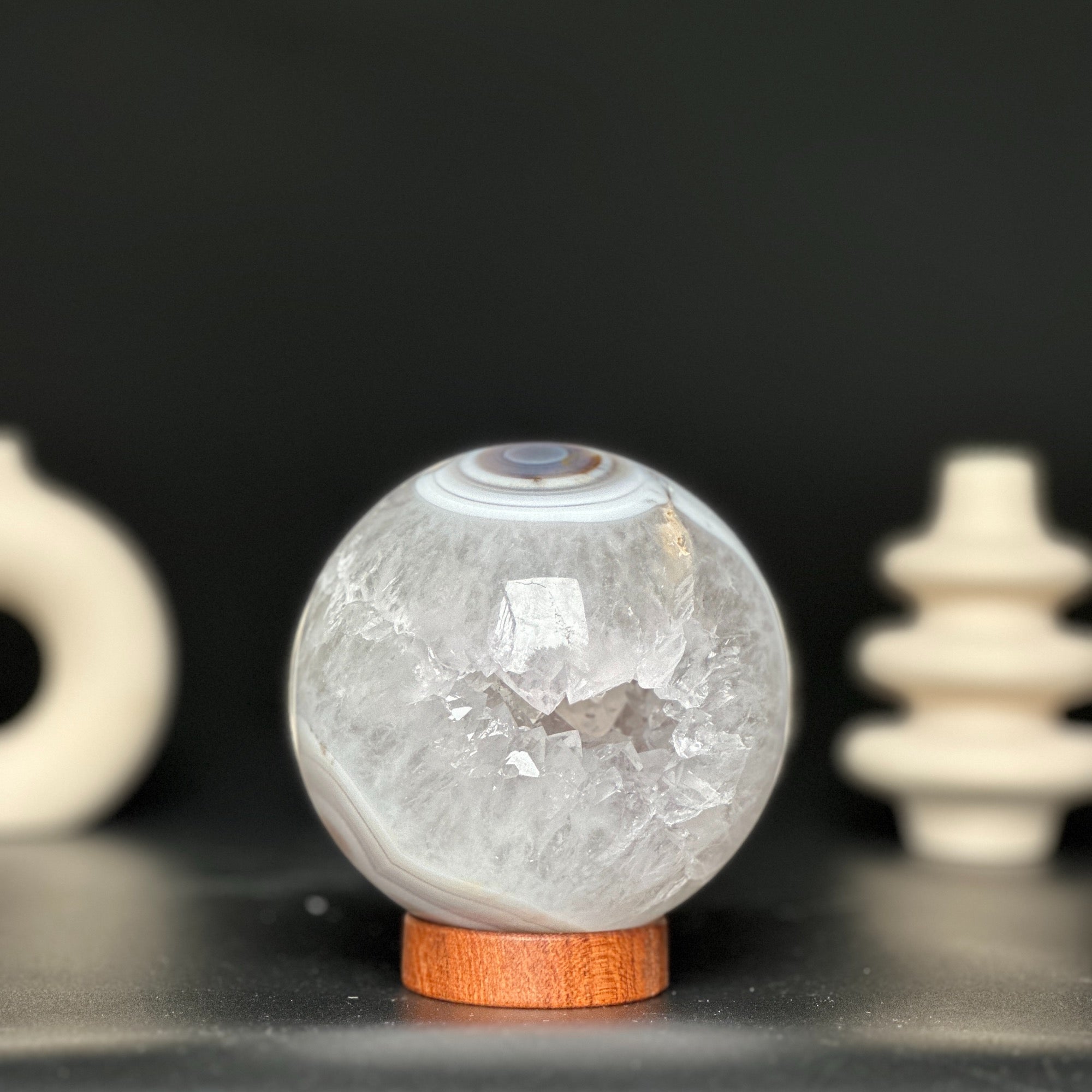 Polished white and beige agate and quartz gemstone sphere on a carob wood base.