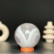 Polished white and beige agate gemstone sphere on a carob wood base.