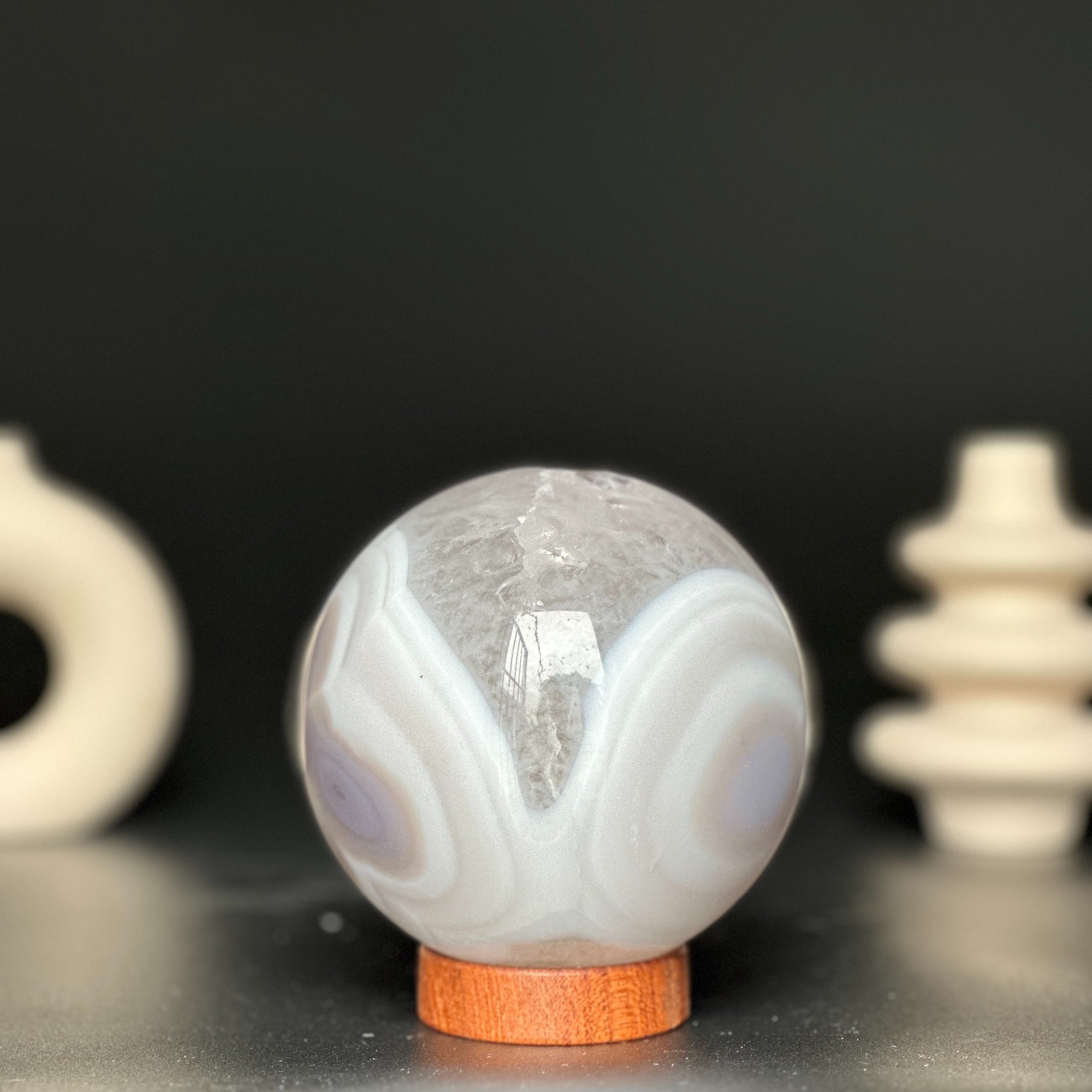 Polished white and beige agate gemstone sphere on a carob wood base.