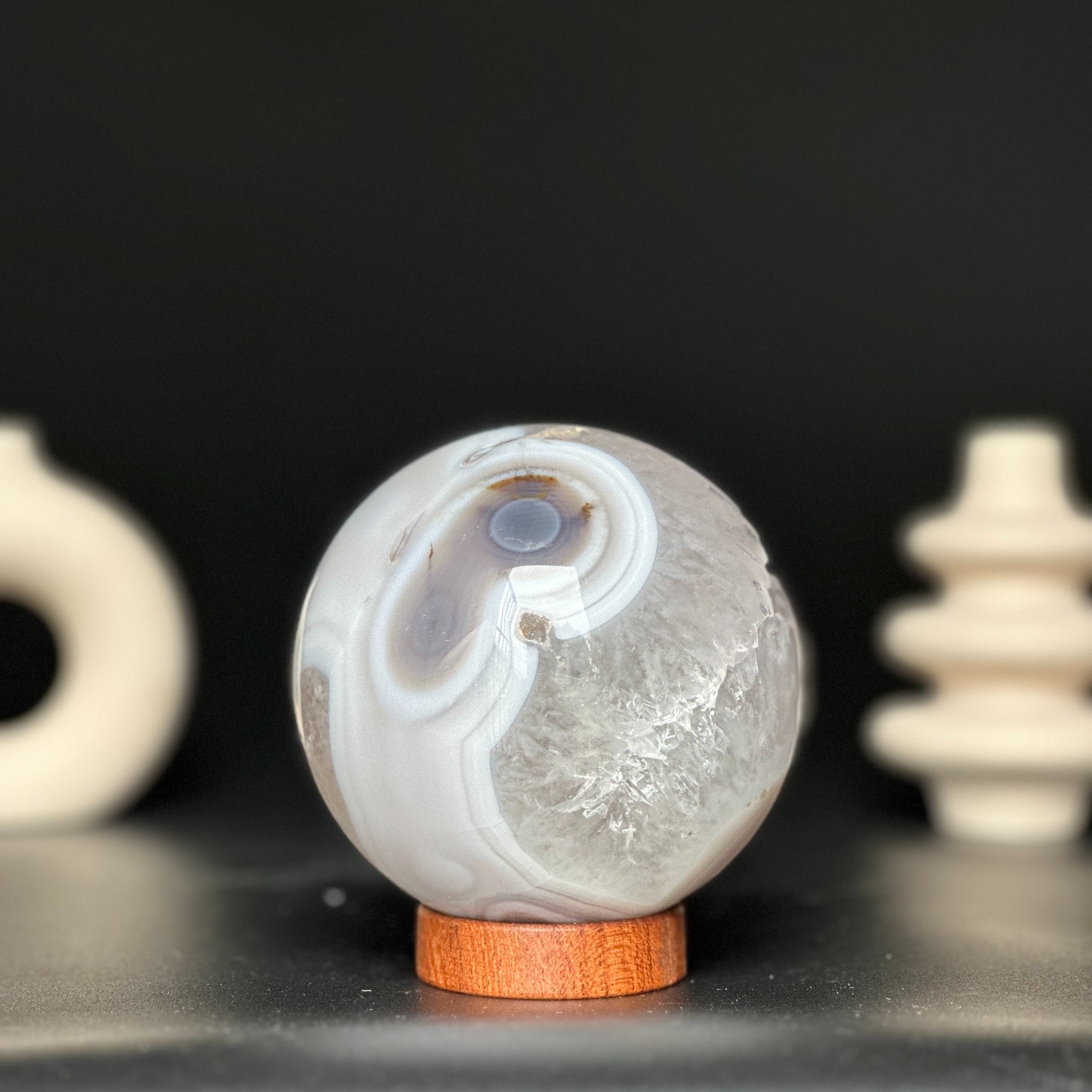 Polished white and beige agate and quartz gemstone sphere on a carob wood base.