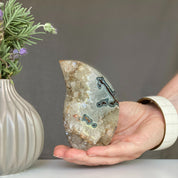 Polished green and red agate flame decor with natural crystals, held in a hand.