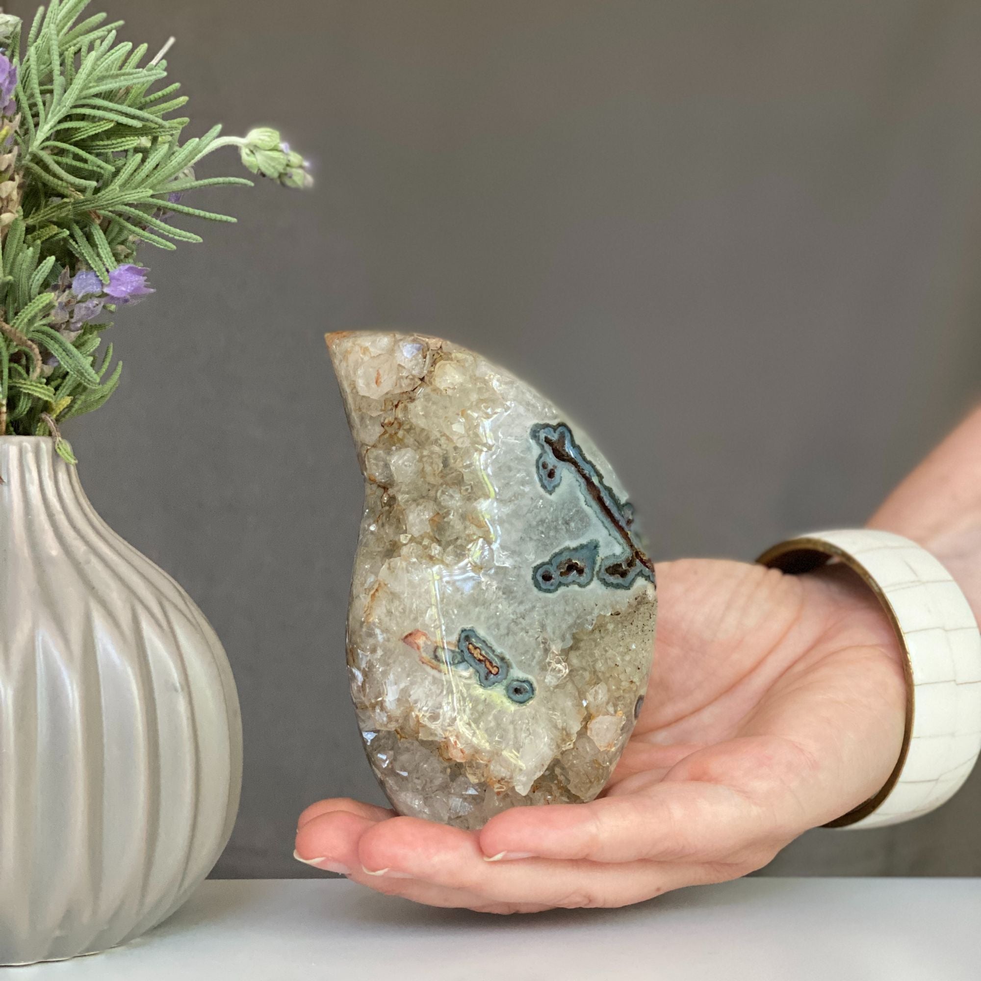Polished green and red agate flame decor with natural crystals, held in a hand.