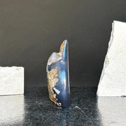 Polished dark blue agate and quartz flame crystal, 5-inch tall, with rough brown edges on a black surface.