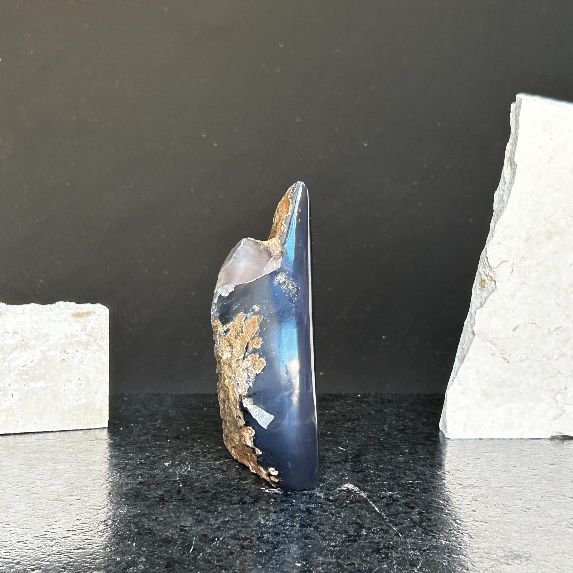 Polished dark blue agate and quartz flame crystal, 5-inch tall, with rough brown edges on a black surface.