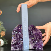 Supersized amethyst geode bookends holding a gray "Kinfolk Travel" book, with hands adjusting.