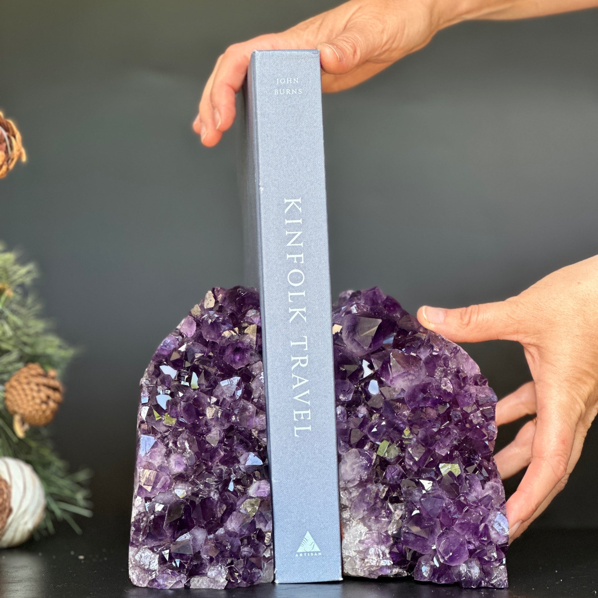 Supersized amethyst geode bookends holding a gray "Kinfolk Travel" book, with hands adjusting.