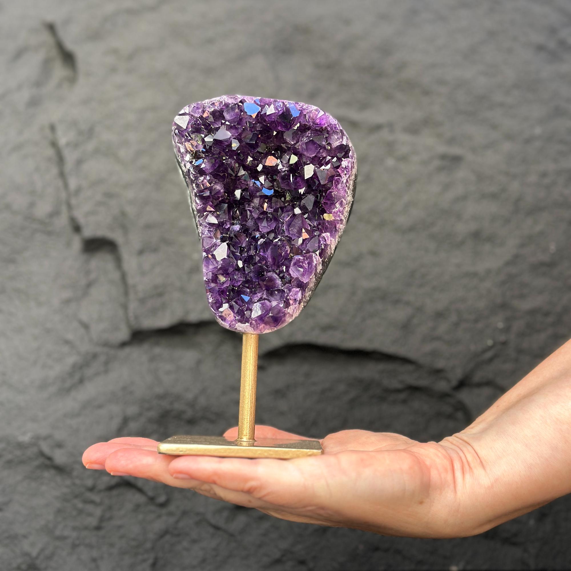 Extra large natural amethyst crystal geode on a gold metal stand, held in a hand.