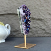 Extra large, natural purple amethyst crystal geode on a sleek gold metal stand.