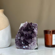 Deep purple Uruguayan amethyst geode cluster, 4-inch tall, next to a beige vase and brown candle.