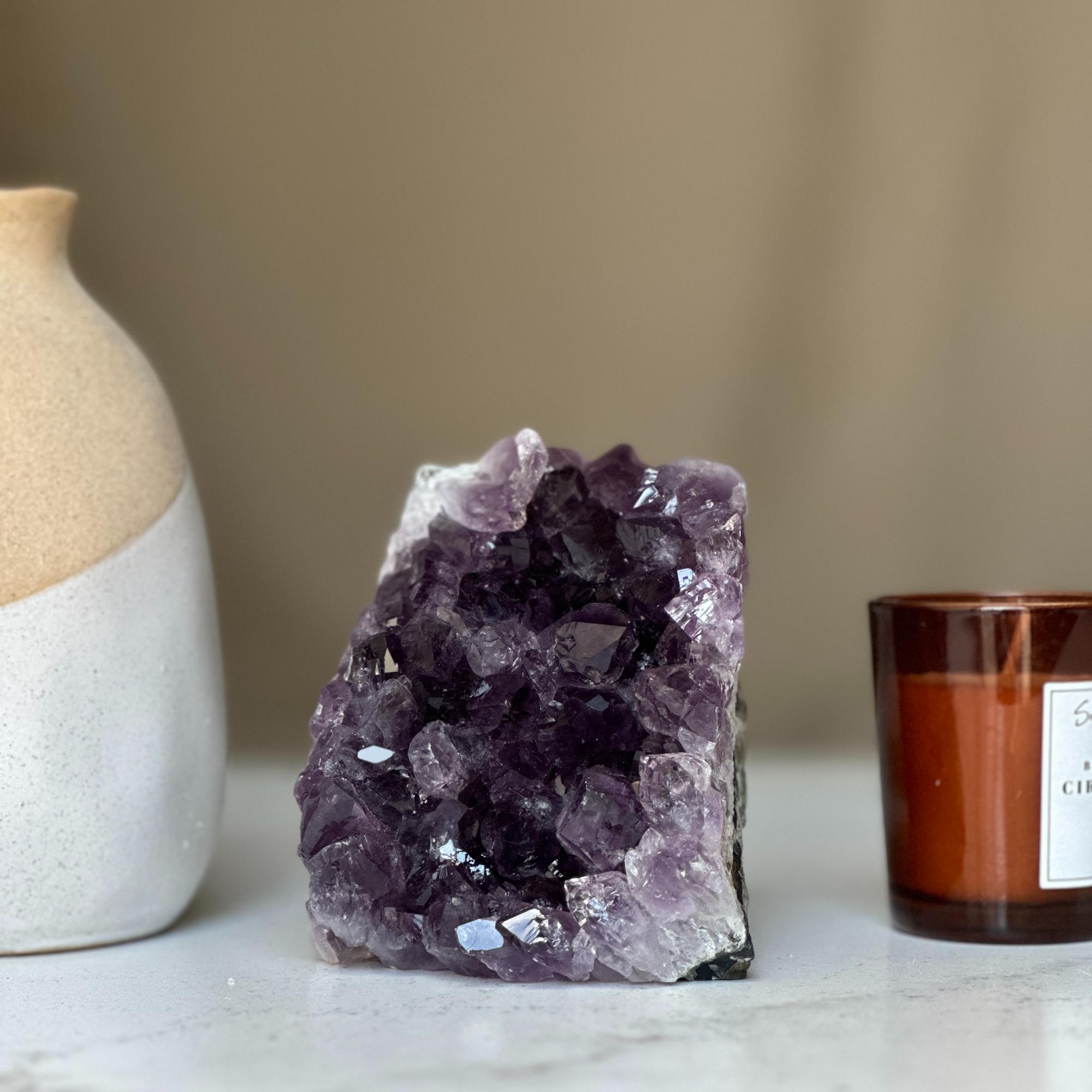 Deep purple Uruguayan amethyst geode cluster, 4-inch tall, next to a beige vase and brown candle.