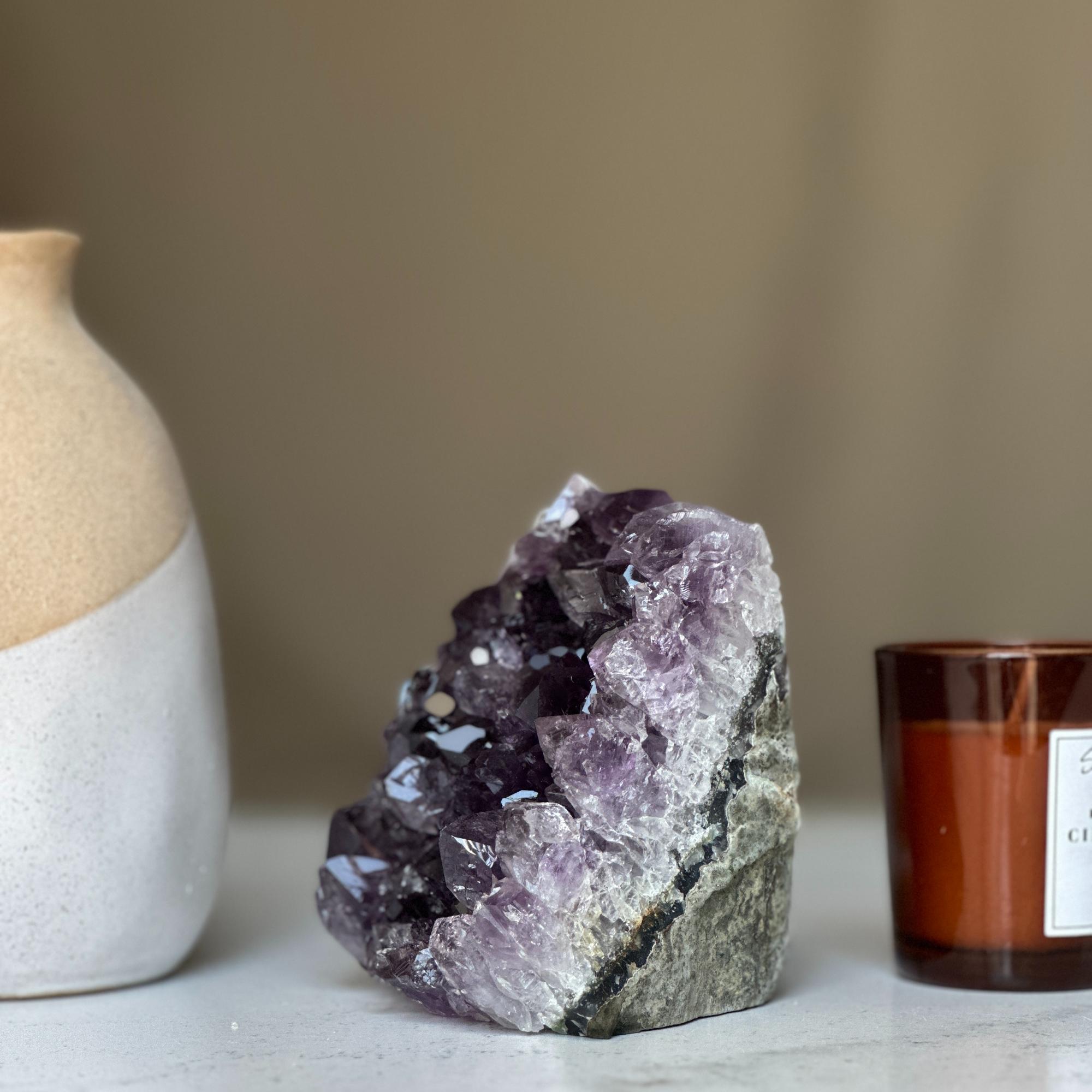 Deep purple amethyst geode cluster from Uruguay, 4-inch tall, next to a beige vase and brown candle.