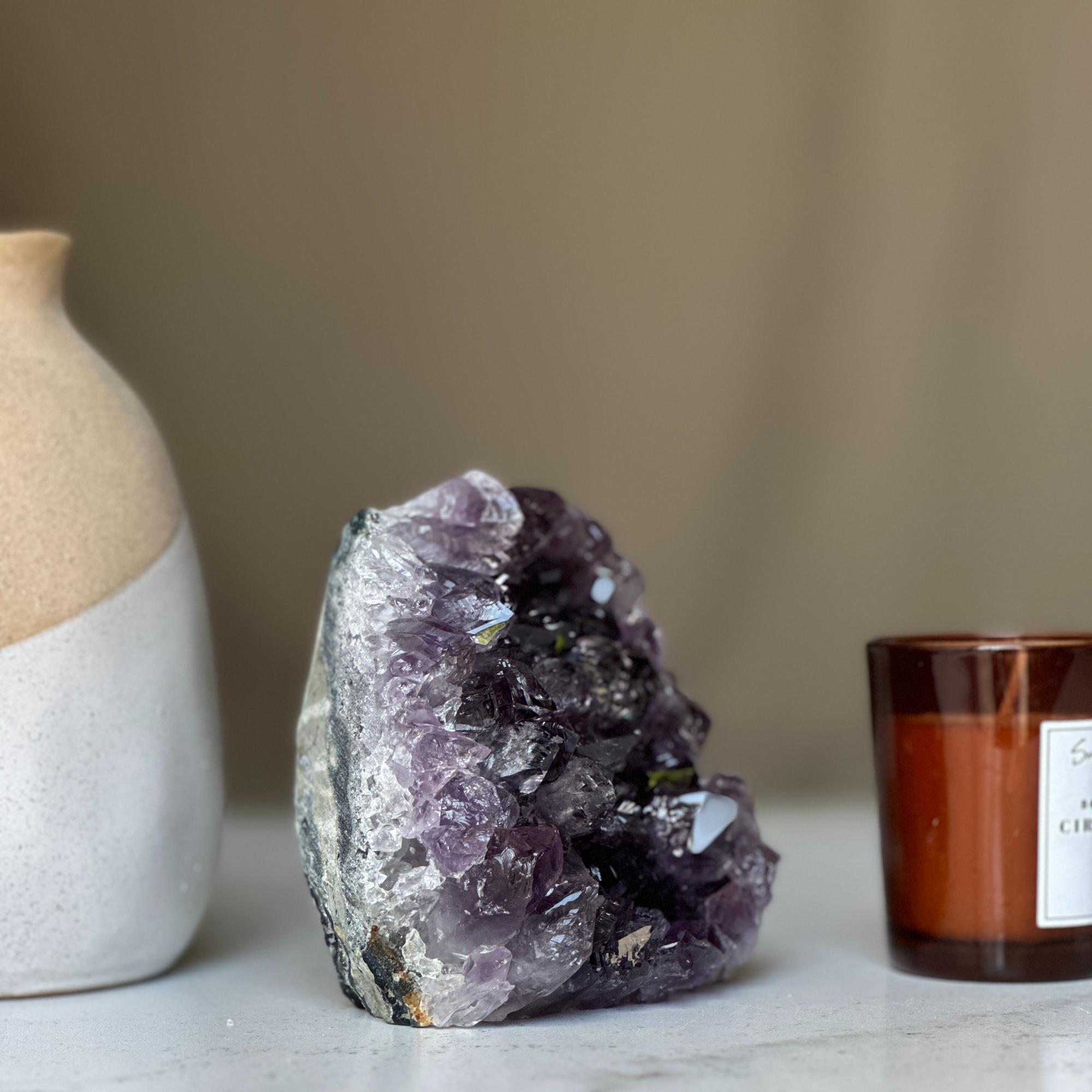 Large deep purple amethyst geode cluster from Uruguay, 4-inch tall, next to a white vase and brown candle.