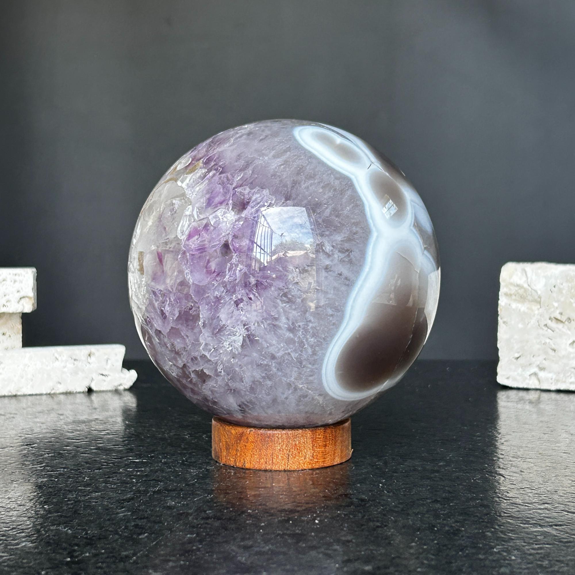 Polished amethyst and agate sphere with gray, brown, and white bands on a carob wood base.