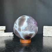 Polished amethyst and agate sphere, 4-inch diameter, with gray, brown, and white patterns on a carob wood base.