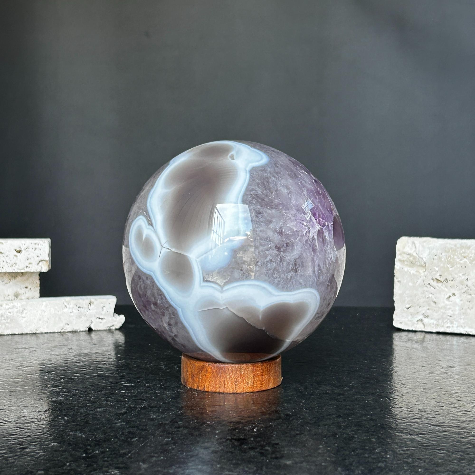 Polished amethyst and agate sphere, 4-inch diameter, with gray, brown, and white patterns on a carob wood base.