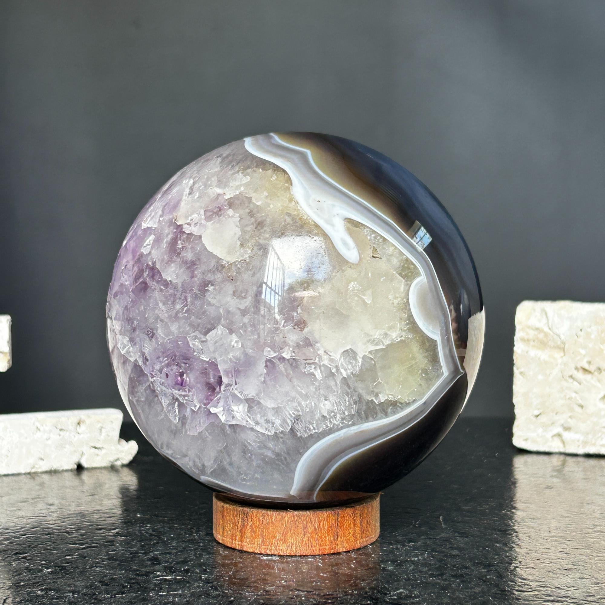 Polished amethyst and agate sphere with gray, brown, and purple geode on a wooden base.