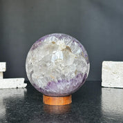 Polished amethyst and agate sphere with clear quartz inclusions on a round carob wood base.