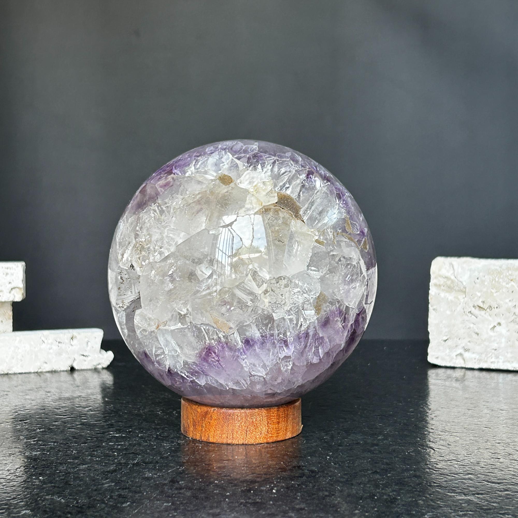 Polished amethyst and agate sphere with clear quartz inclusions on a round carob wood base.
