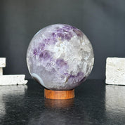 Polished amethyst and agate crystal sphere on a carob wood base, showing purple, gray, and white formations.