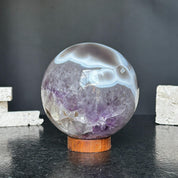 Polished amethyst and agate sphere with gray, brown, and white bands on a round carob wood base.