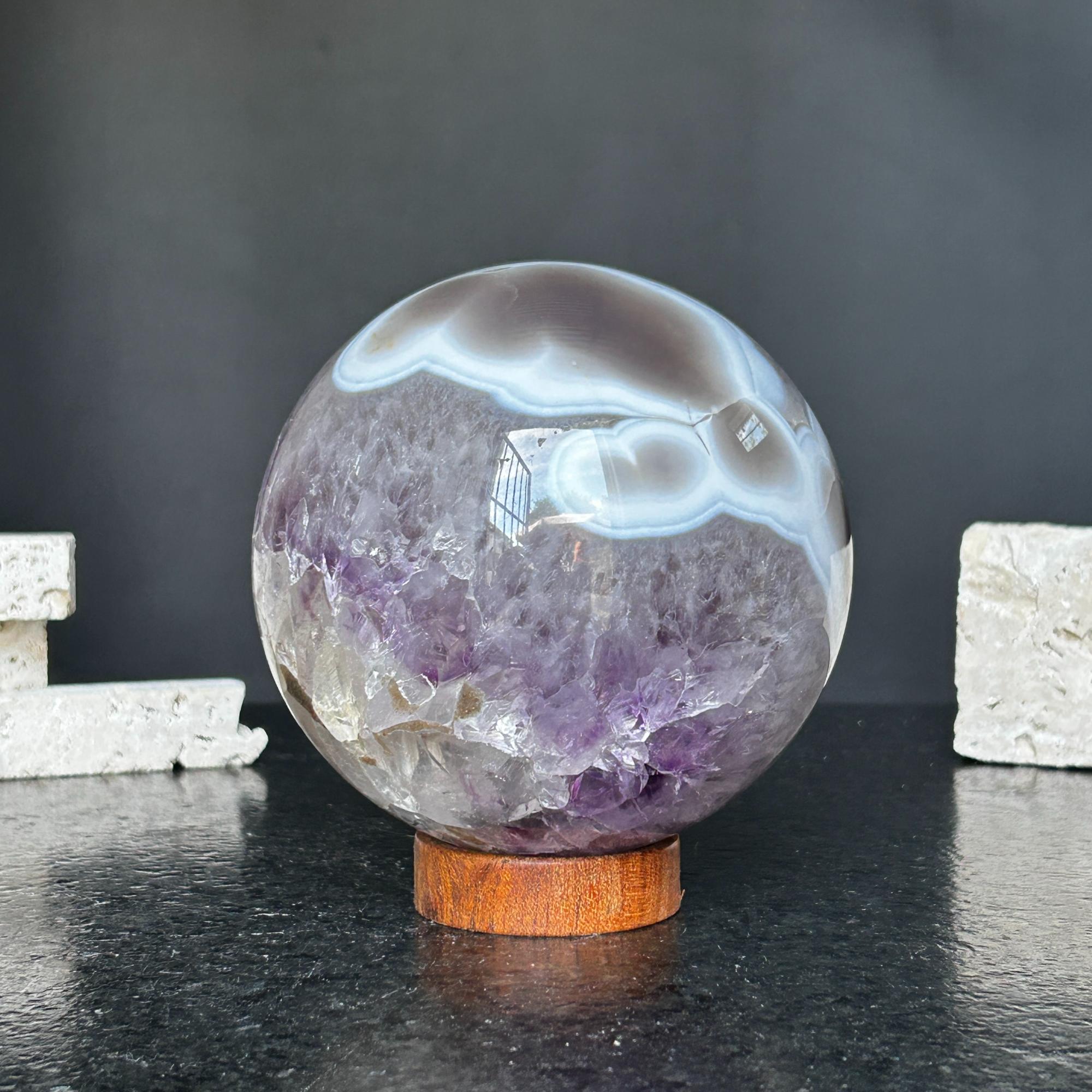 Polished amethyst and agate sphere with gray, brown, and white bands on a round carob wood base.