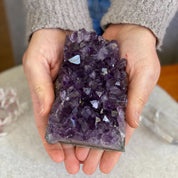 Hands holding a vibrant purple amethyst and agate cluster, 4.5 inches tall, for home decor.