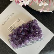 Vibrant purple amethyst and agate cluster, 3x4.5 inch, on a book, with pink flowers.