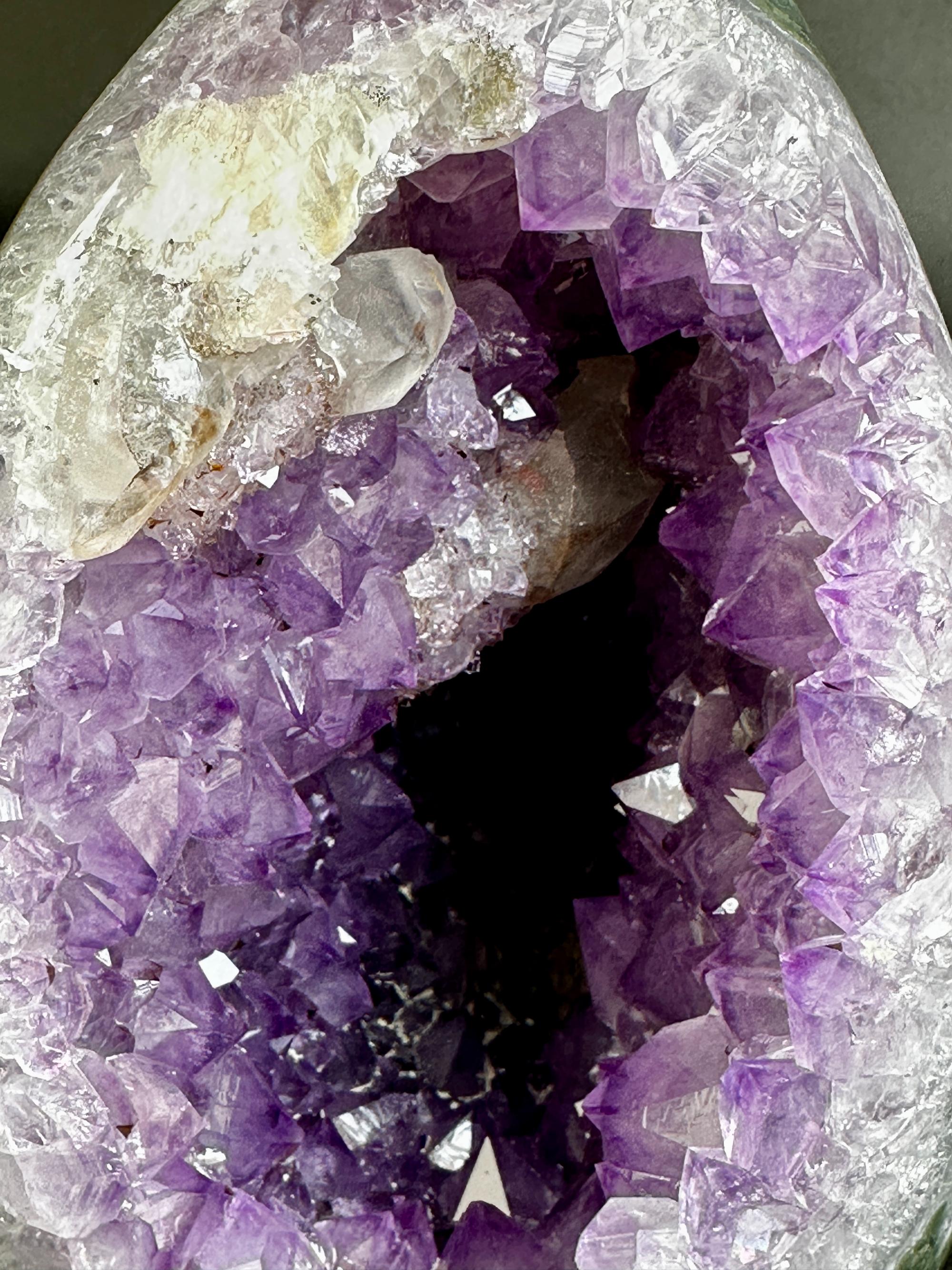A close-up of a geode-like crystal formation with a purple amethyst interior, clear quartz crystal points, and a dark central cavity.