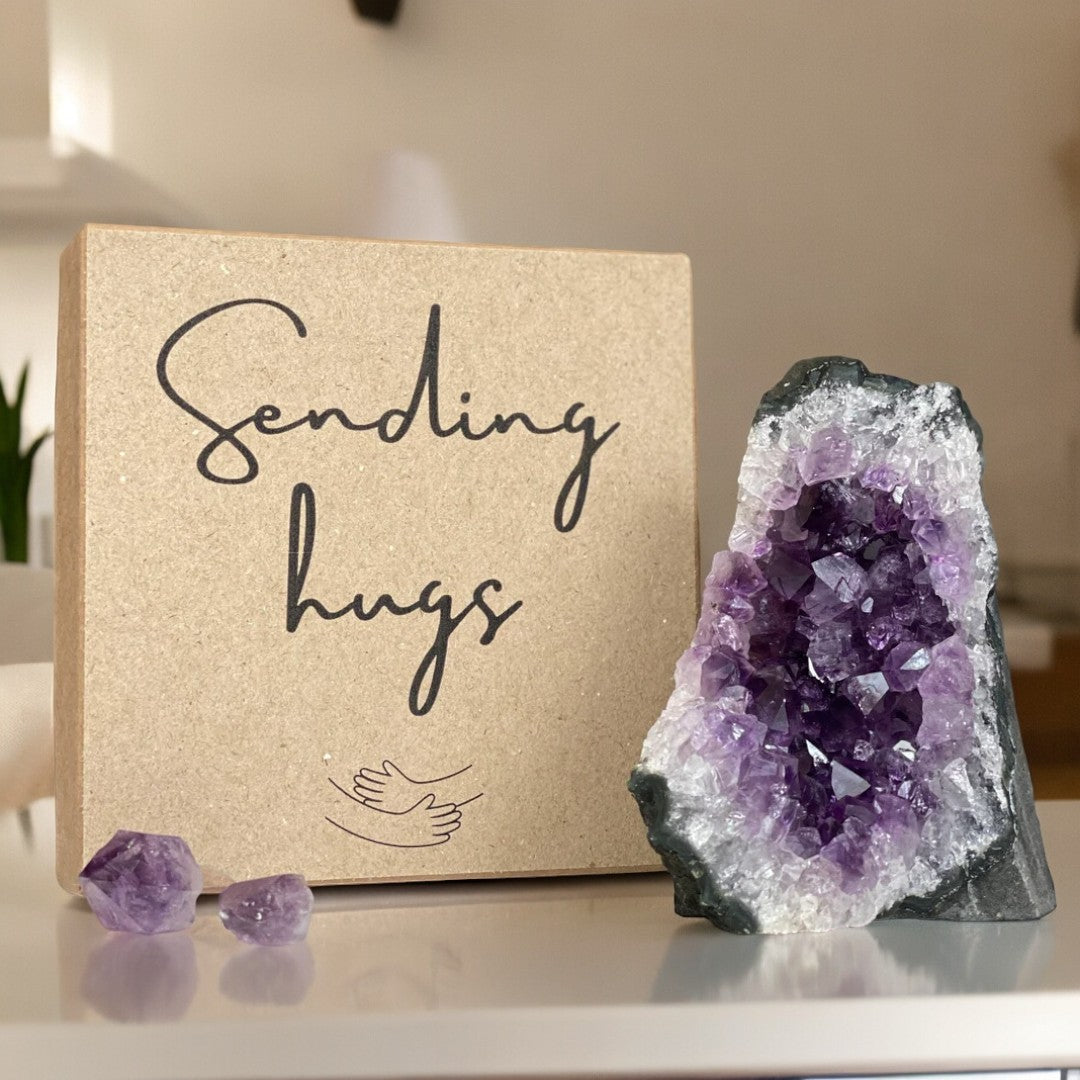 Rigid kraft "Sending hugs" gift box with a vibrant purple amethyst geode and two small raw crystals.