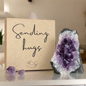 Rigid kraft "Sending hugs" gift box with a vibrant purple amethyst geode and two small raw crystals.