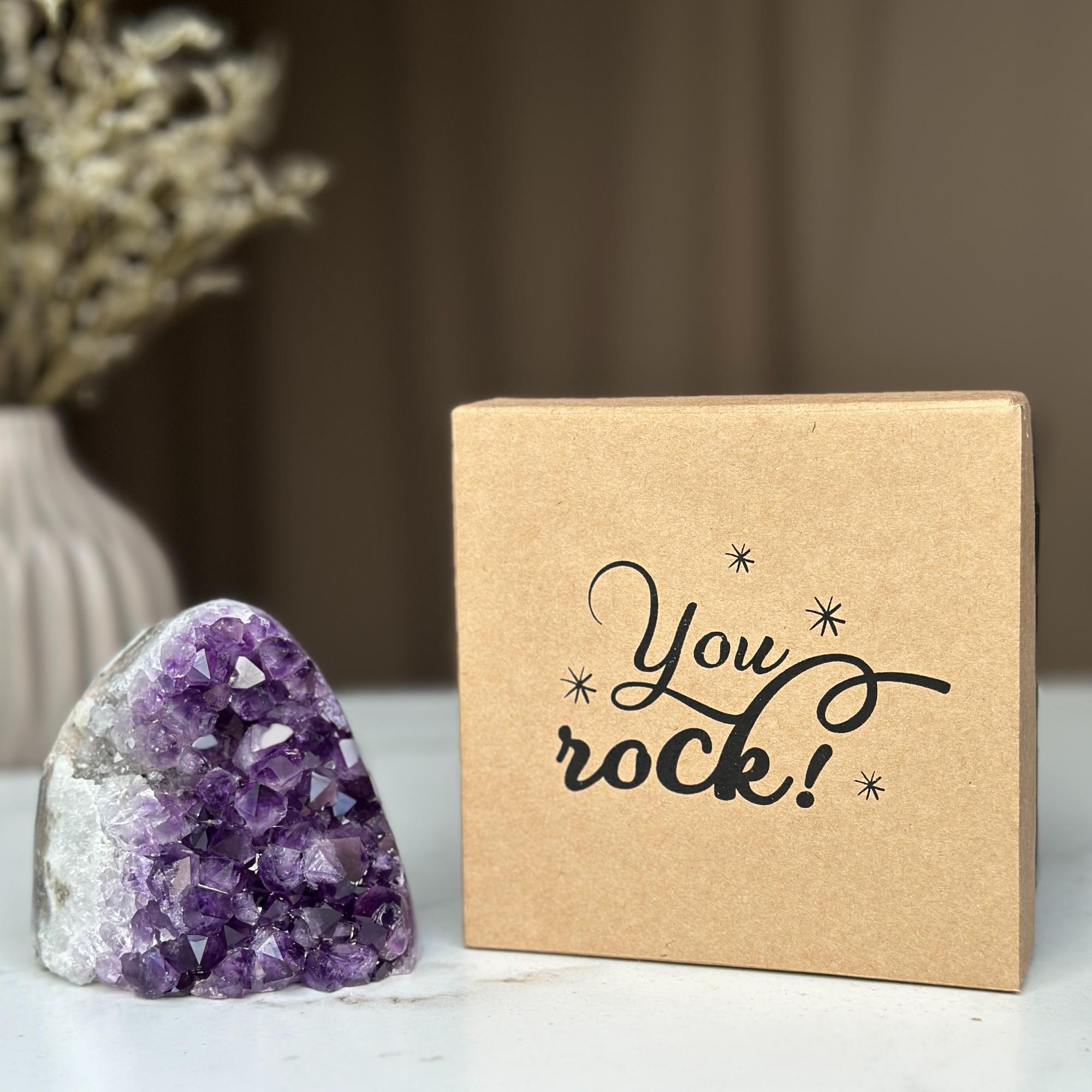 Sparkling purple amethyst geode and a brown kraft gift box with "You rock!" text, ideal anniversary gift.