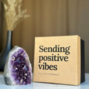 Sparkling purple amethyst geode beside a rigid kraft anniversary gift box with "Sending positive vibes" text.