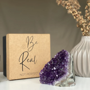 Vibrant purple amethyst geode with sparkling crystals next to a kraft "Be Real" premium anniversary gift box.
