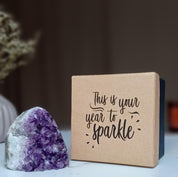 Amethyst geode crystal next to a brown gift box with "This is your year to sparkle" in black script.