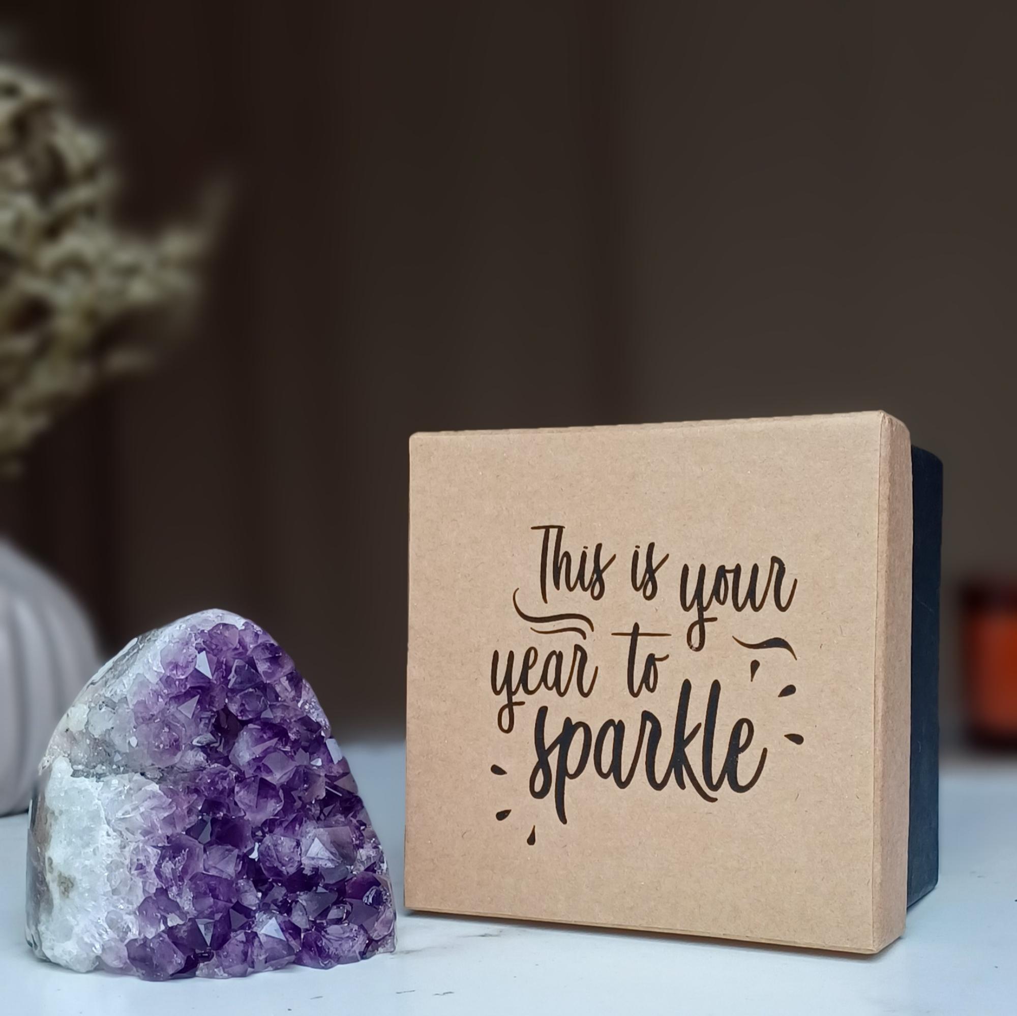 Amethyst geode crystal next to a brown gift box with "This is your year to sparkle" in black script.