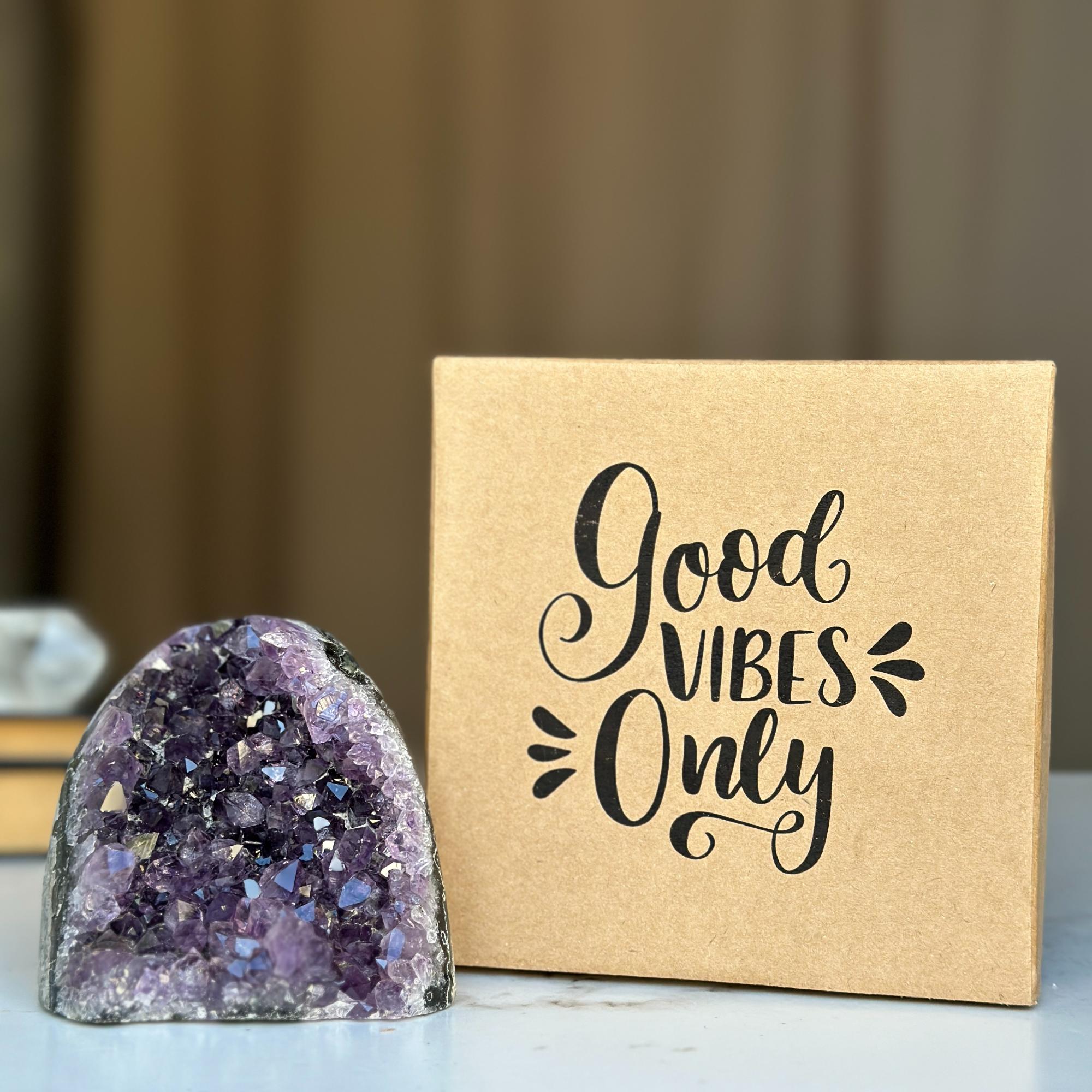 Amethyst geode crystal next to a brown gift box with "Good Vibes Only" in black script.