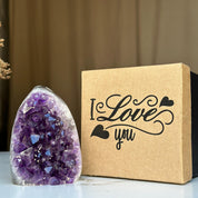 Polished deep purple amethyst geode with white base next to a kraft brown "I Love you" anniversary gift box.