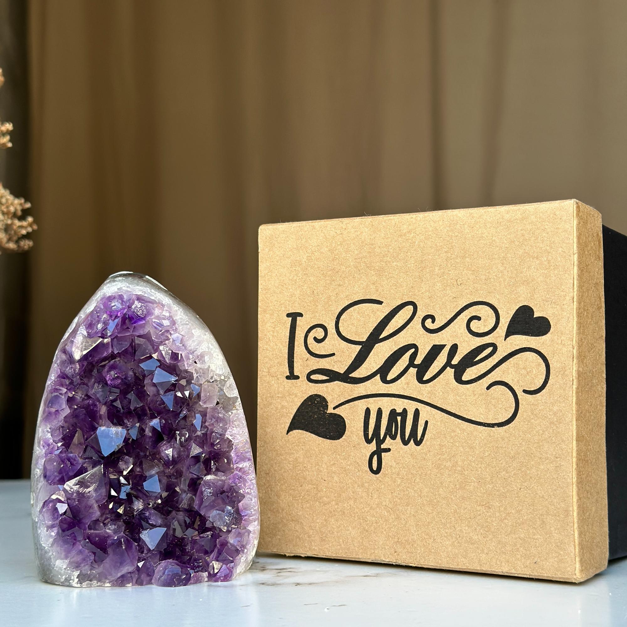 Polished deep purple amethyst geode with white base next to a kraft brown "I Love you" anniversary gift box.