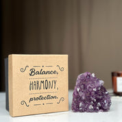 Kraft gift box with "Balance, HARMONY, protection" text, next to a raw, vibrant purple amethyst crystal cluster.