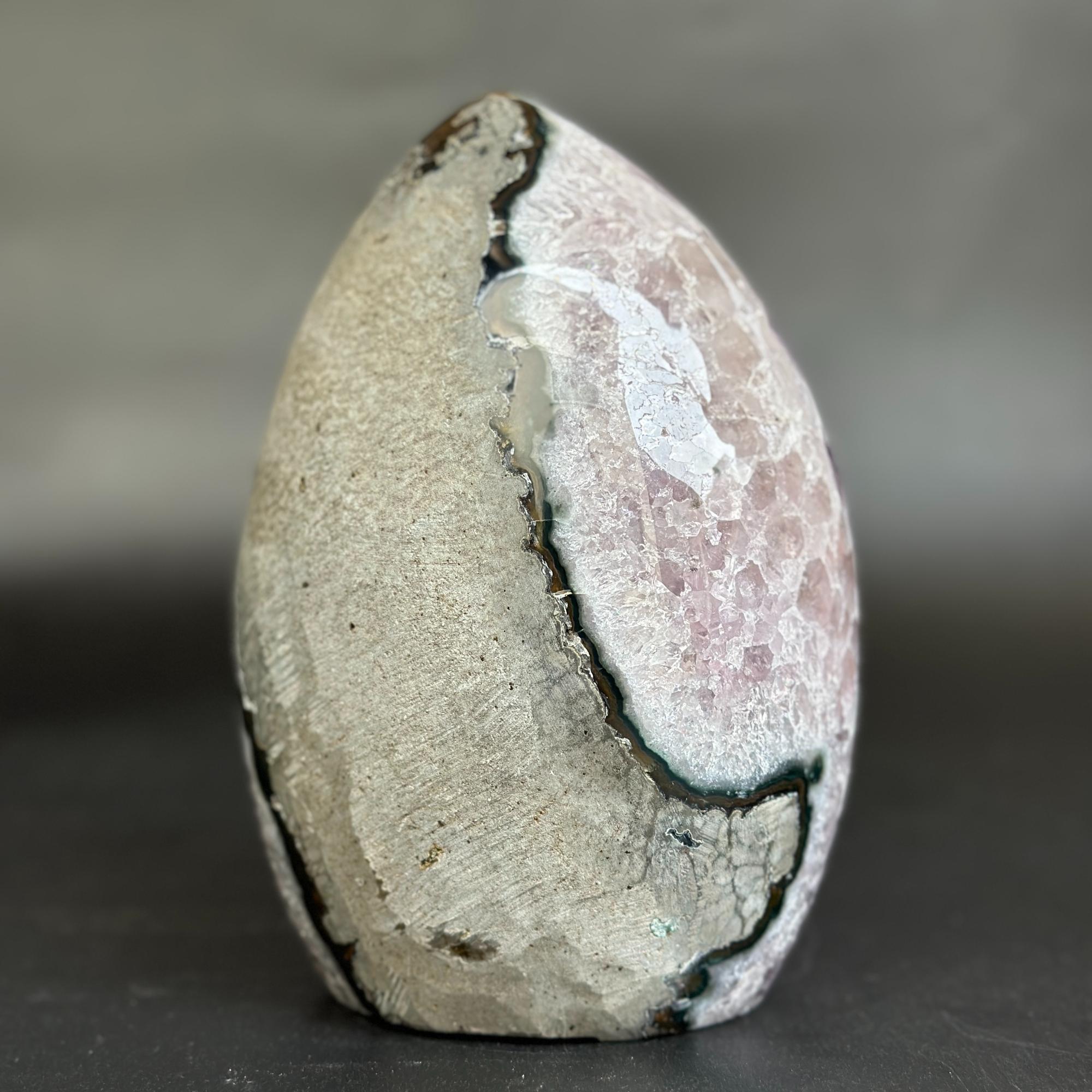 A polished pink rose quartz crystal egg with a natural dark fissure running vertically down the center, set against a dark gray background.