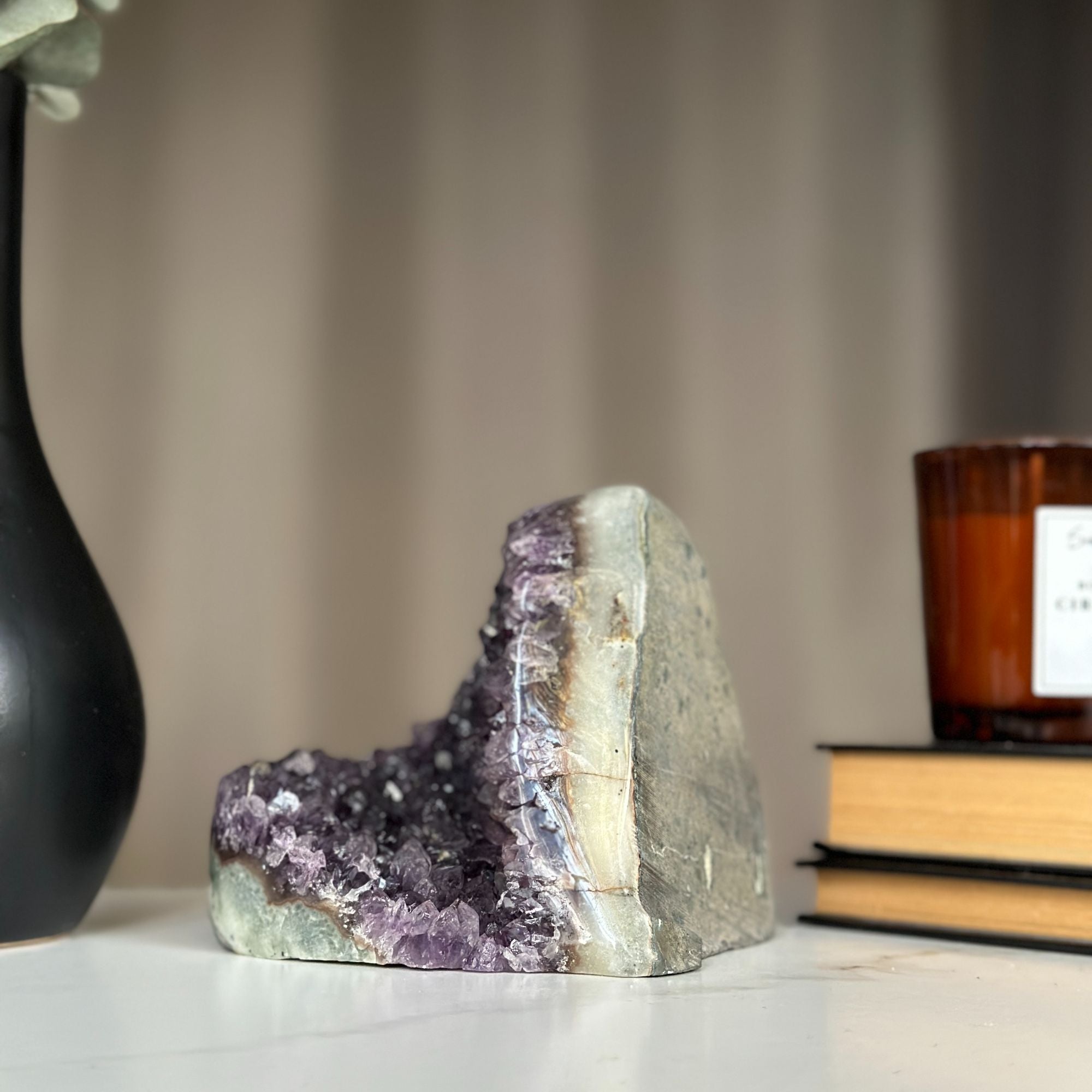 Large, shiny amethyst cluster with huge purple crystals, displayed next to a black vase and books.