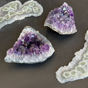Two deep purple amethyst geode clusters and two white and green agate slices on a dark surface.